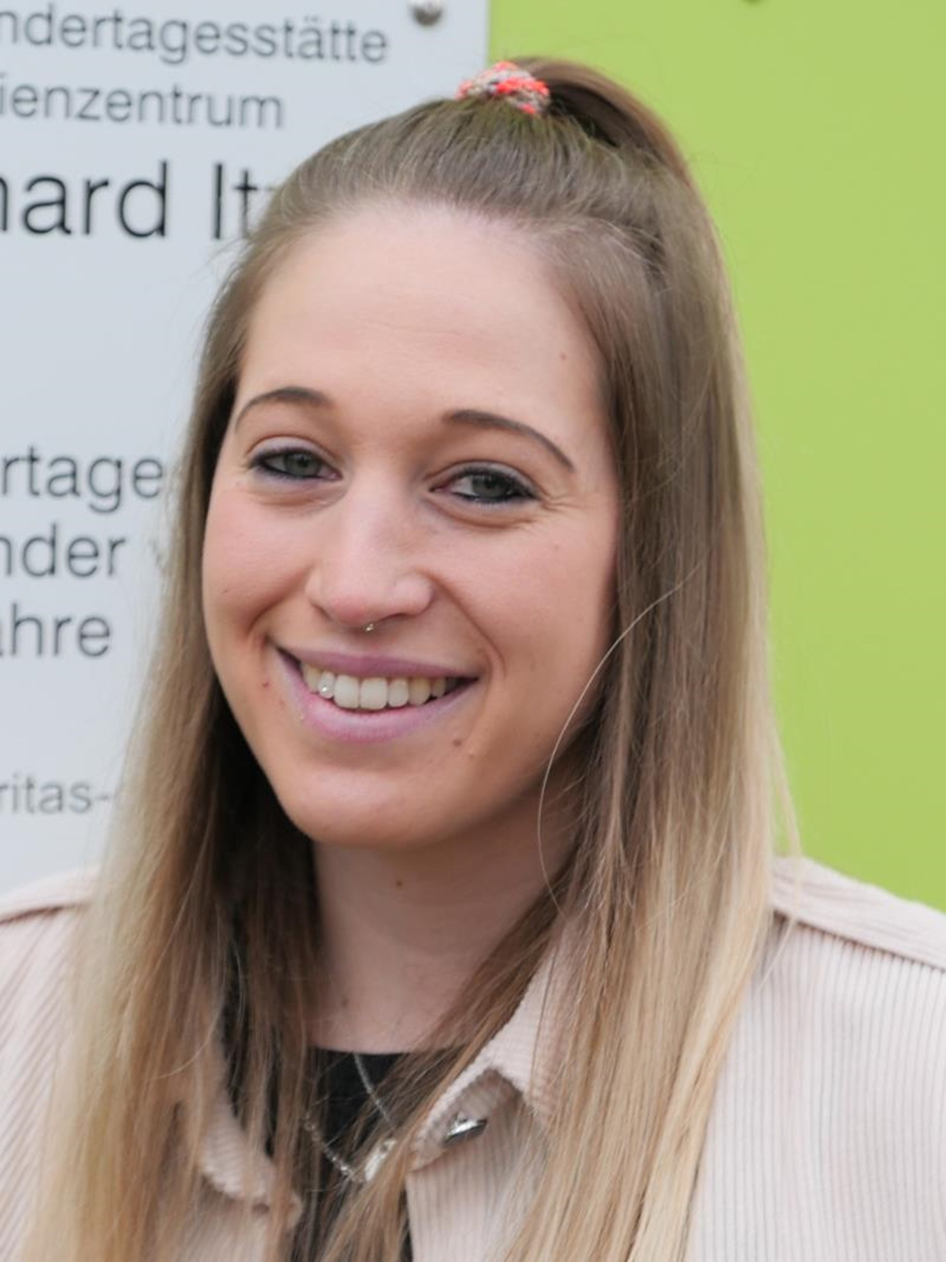 Junge Frau mit langen blonden Haaren vor einem Caritas-Schild.